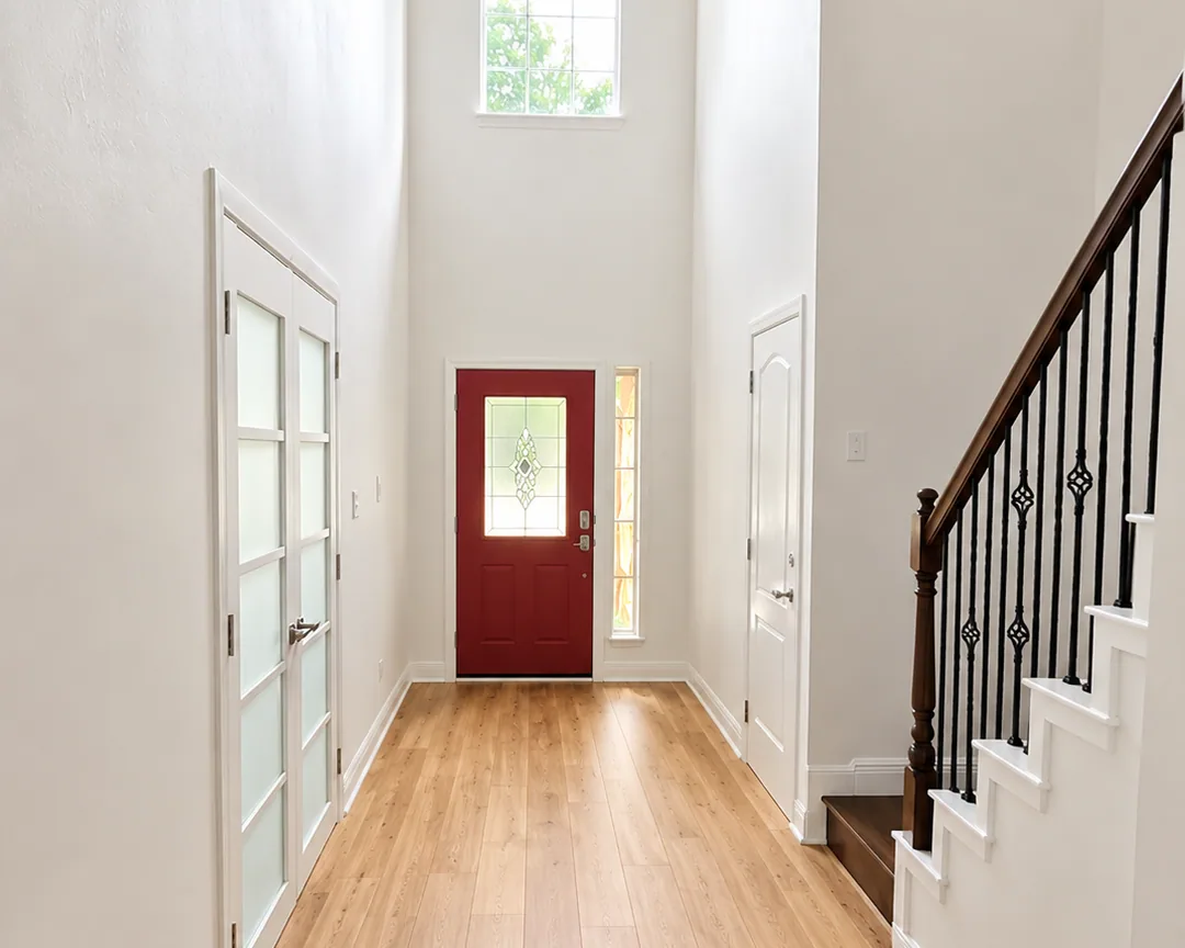 Bright remodeled foyer with white walls, wood flooring, staircase, and red front door