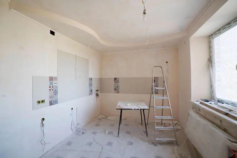 Kitchen renovation in progress with ladder, tile work, and protected floors
